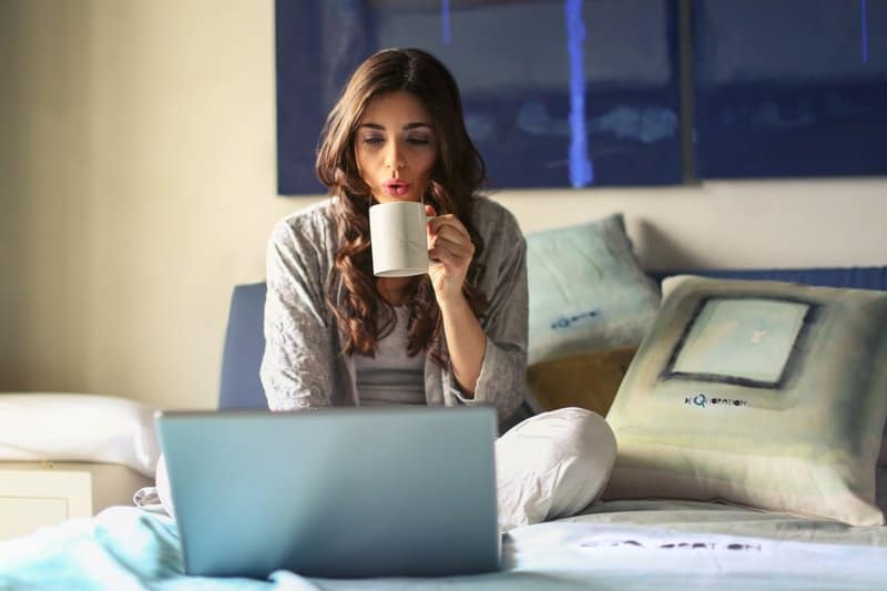 kvinna i grå jacka med sin bärbara dator när man sitter på sängen