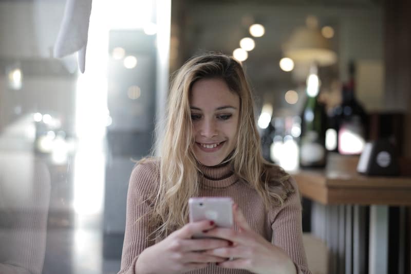 woman with brown turtle-neck shirt looking at the phone