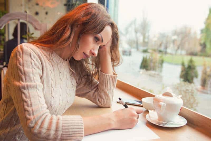 sorglig kvinna som skriver brev på kaffebaren