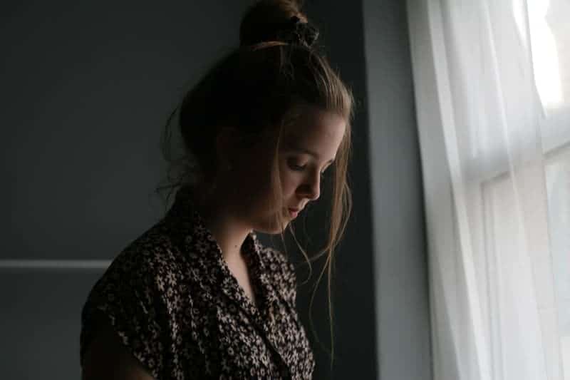 sorglig ung kvinna som står vid fönstret