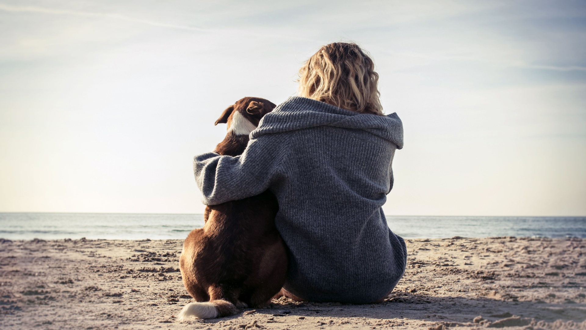 kvinna och hund sitter pae en strand