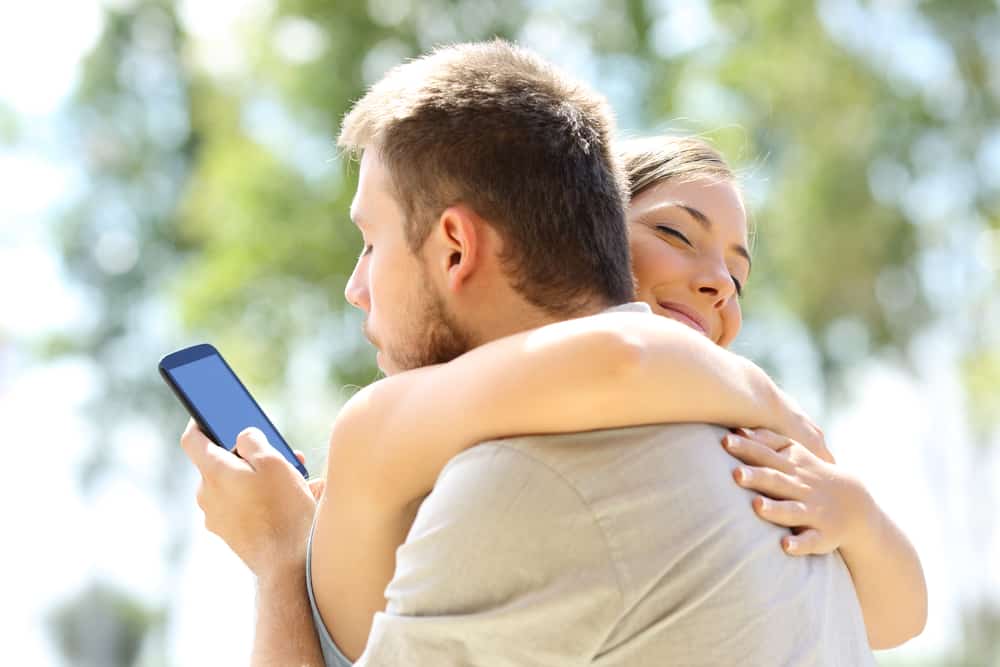 kvinna kramar man medan man tittar på mobil
