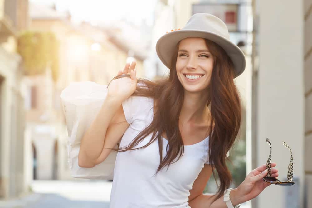 kvinna med hatt som håller solglasögon i handen