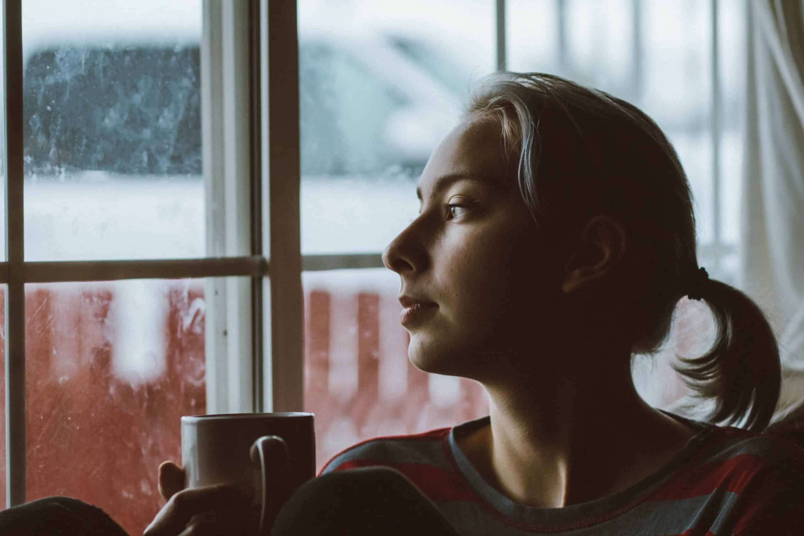 kvinna med kaffekoppen som ser genom fönstret
