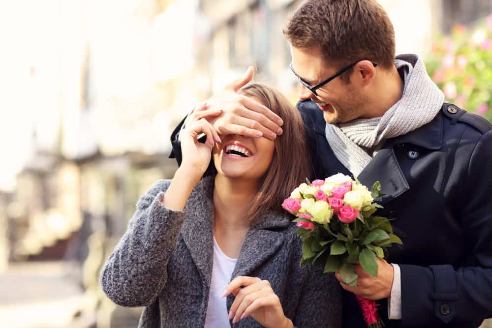 man stänger kvinnans ögon och överrasker henne med blommor