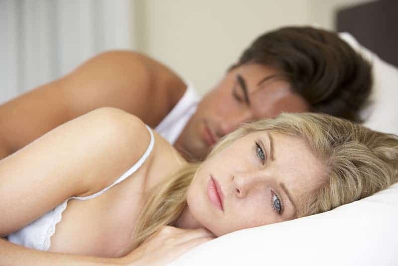 sorglig blond kvinna som ligger i sängen bredvid sin pojkvän som sover