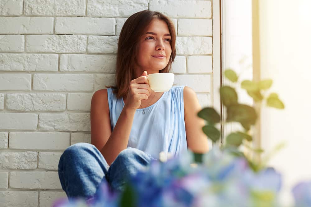 ung glad kvinna som dricker kaffe och tittar utanför