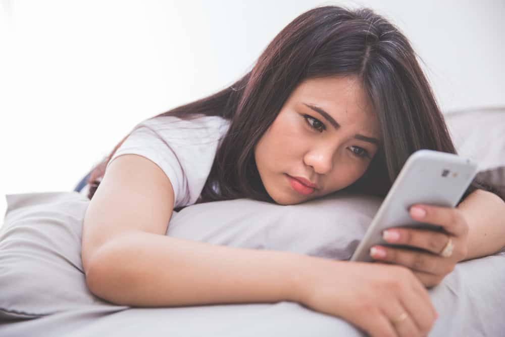 Kvinna som använder mobiltelefonen, medan ligga på sängen