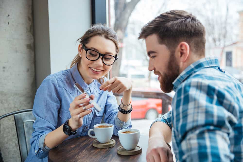 Lyckliga par som tillsammans använder smartphonen och dricker kaffe i kafé