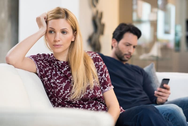sorglig kvinna som sitter pae en soffa som vaender henne tillbaka till en man