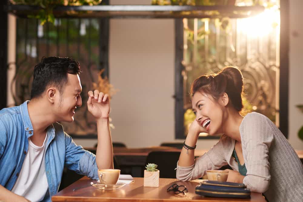 Sidovyståenden av skrattande par som tycker om datum i kafé