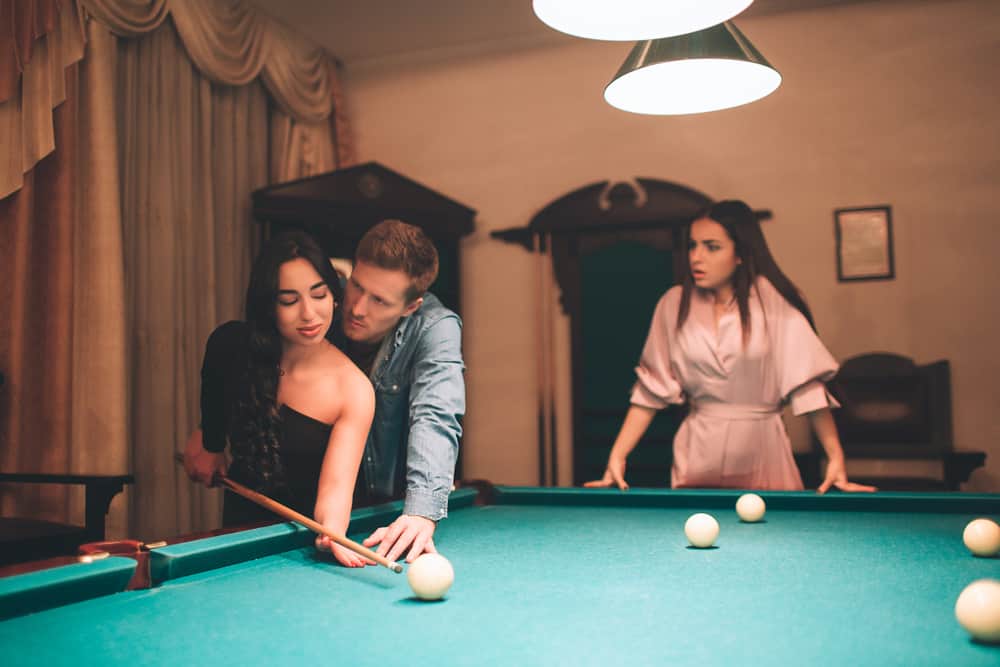 Sjalu kvinna som spelar pool med en annan kvinna och man