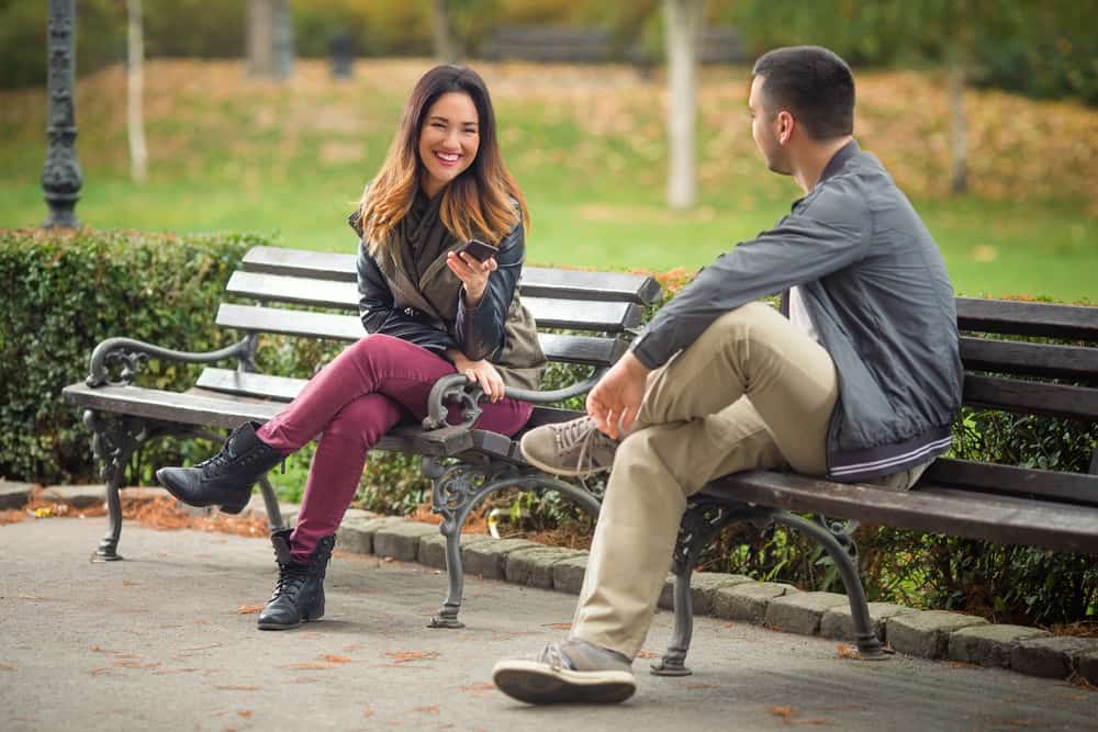Två ungdomar som sitter på bänkar i en park och pratar