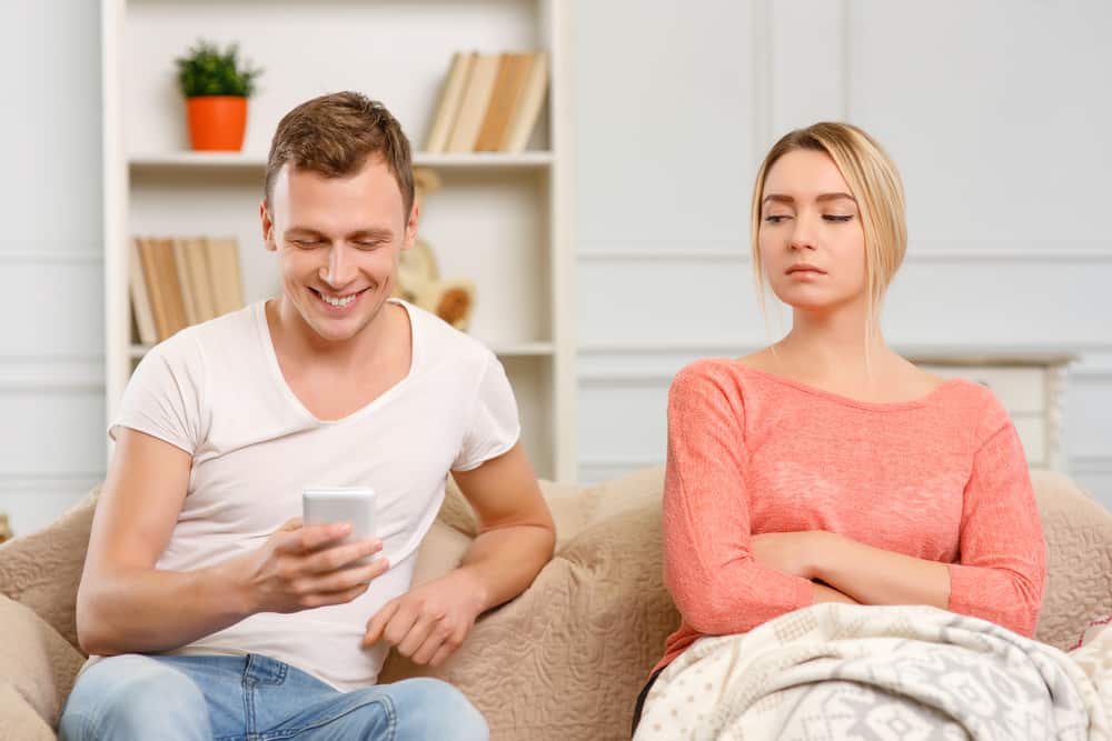 Ung kvinna ser misstänkt ut medan hennes pojkvän smsar på smarttelefonen