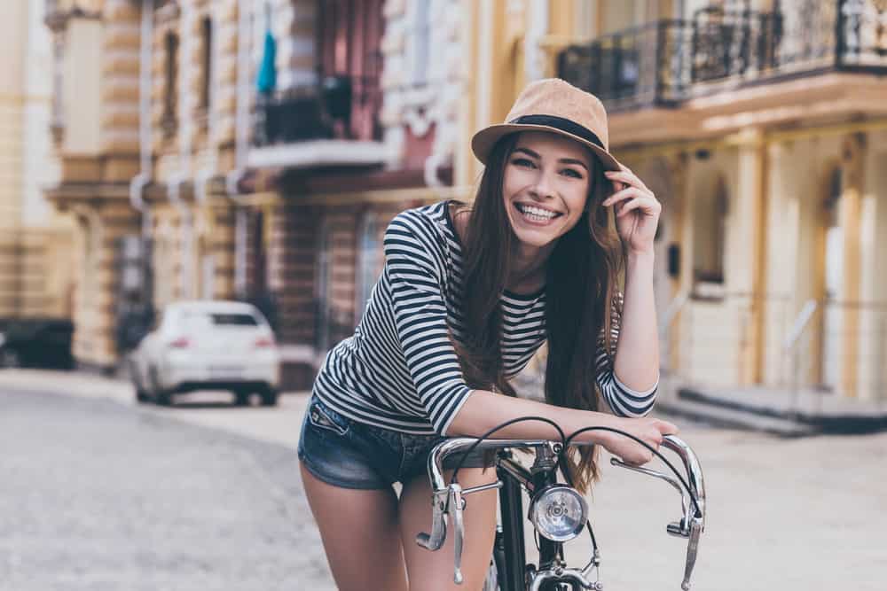Vacker ung kvinna som lutar sig på sin cykel och ler medan du står utomhus
