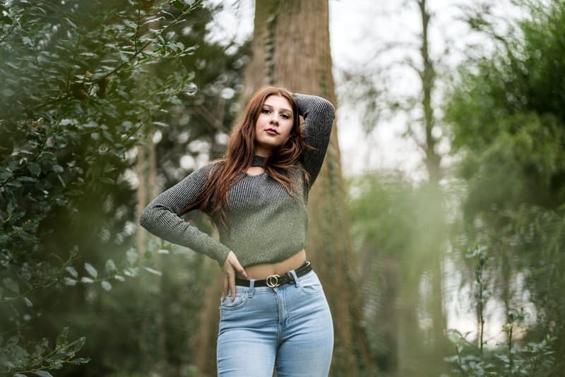 en attraktiv kvinna i jeans och en grå T-shirt står i skogen