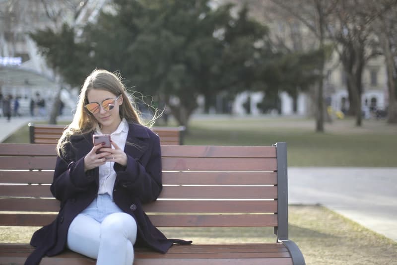 en flicka med solskyddsmedel sitter på en parkbänk och smsar