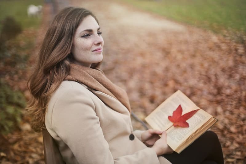 en kvinna som sitter i en park på en bänk med en bok i händerna och tänker