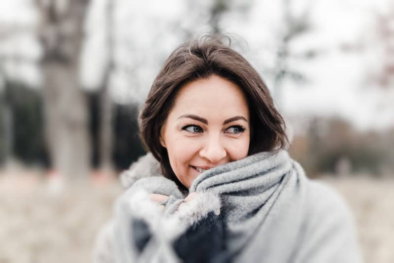 en leende blåögd kvinna står insvept i en filt