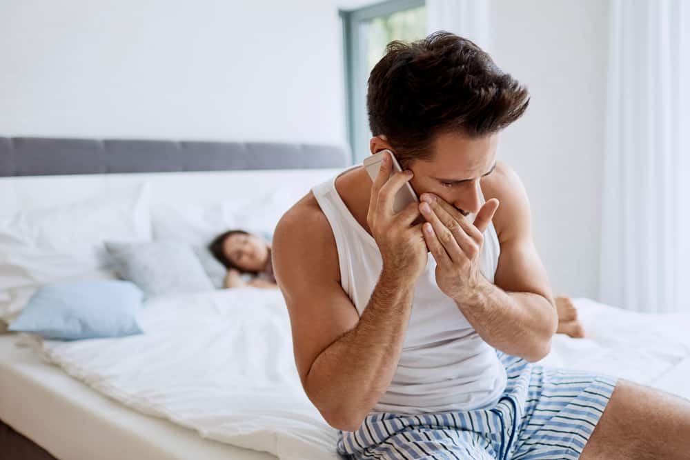 en man i underkläder som pratar tyst på sin mobiltelefon bredvid en sovande kvinna