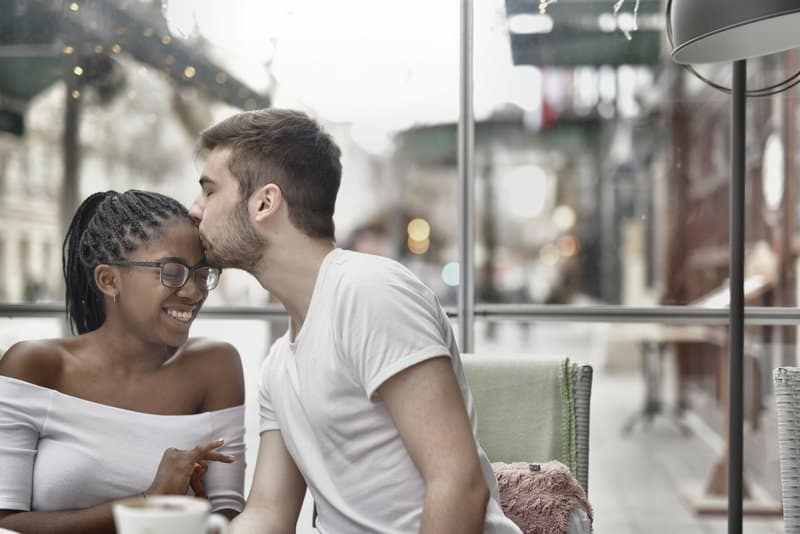 en man kysser en leende svart kvinna på pannan