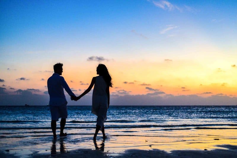 en man och en kvinna som håller händer och går längs stranden