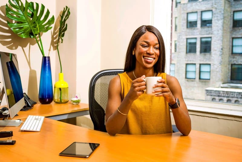 en svart kvinna som sitter vid ett bord och dricker kaffe och skrattar