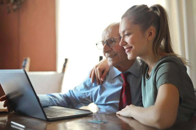 en ung kvinna med ett leende hjälper en äldre man att använda en bärbar dator