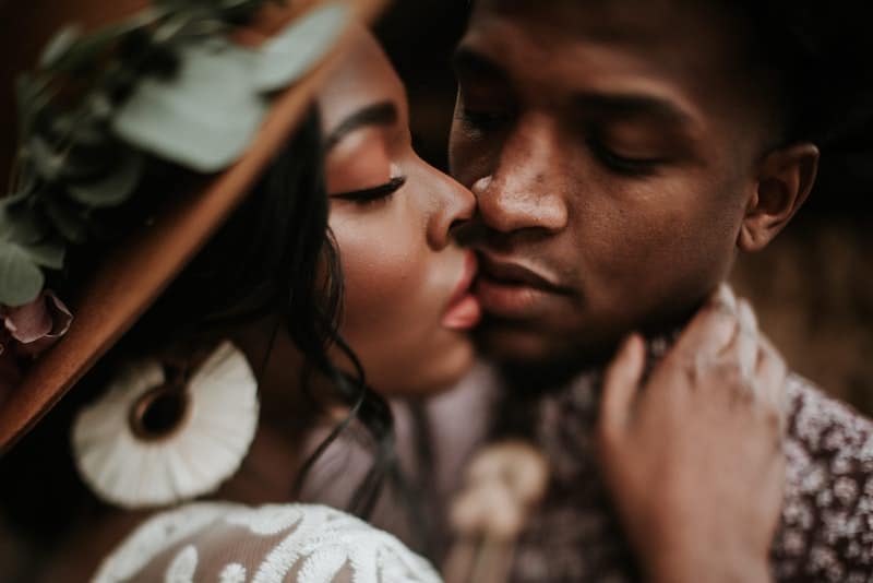 ett fotografi av en svart kvinna i en hatt som ömt kysser hennes man