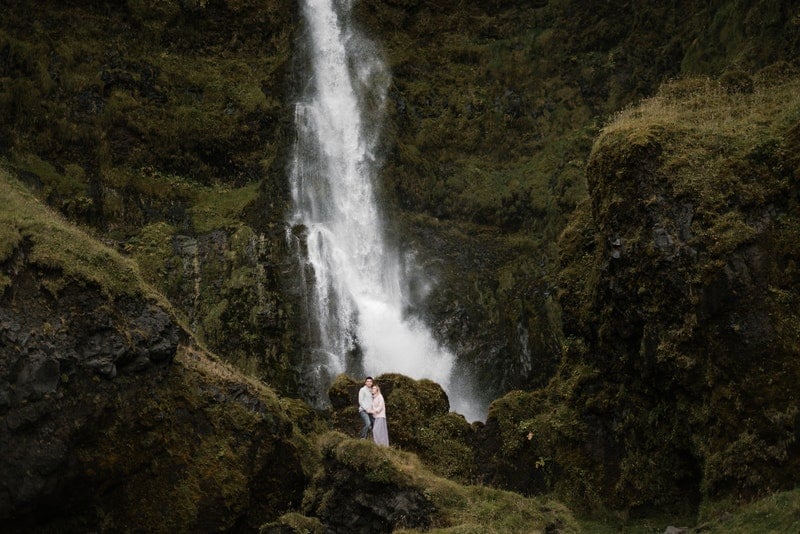 ett fotografi av ett vattenfall under vilket en man och kvinna står i ett omfamning