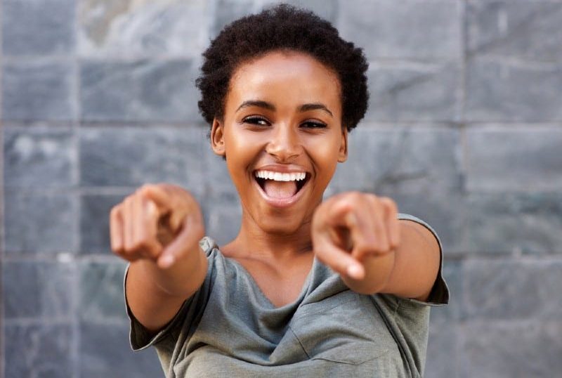 Stående av den attraktiva lyckliga unga svarta kvinnan som pekar fingrar