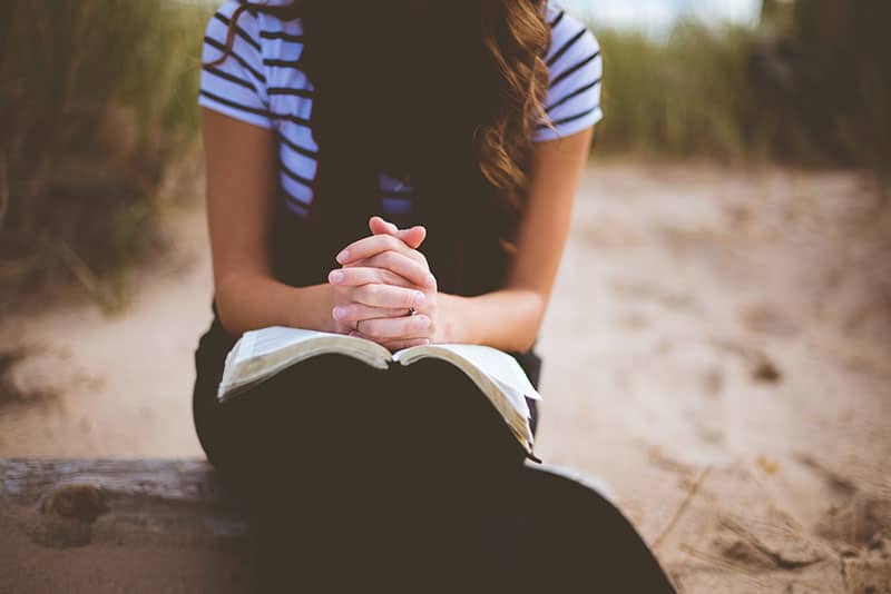 kvinna som ber med bibeln på knä