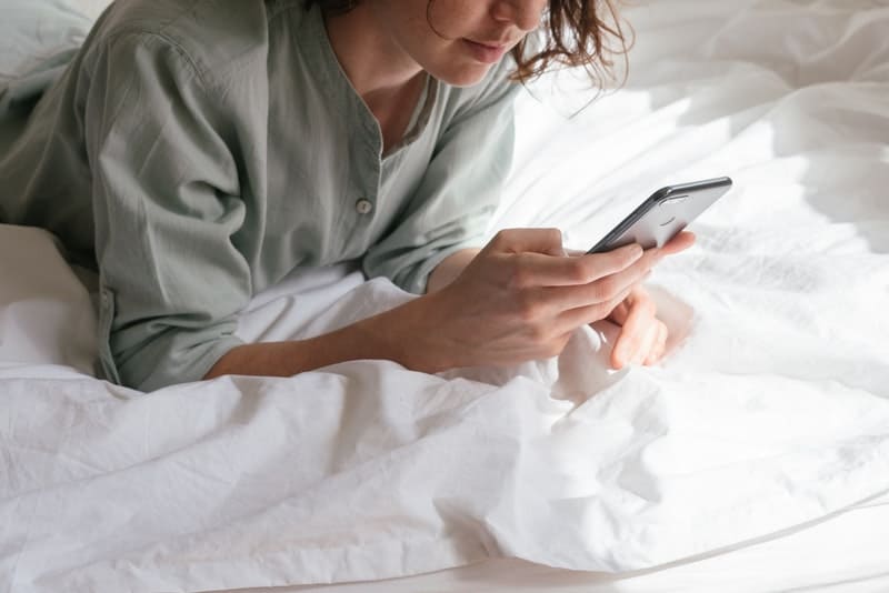 kvinnan ligger på sängen och skriver något på sin mobiltelefon