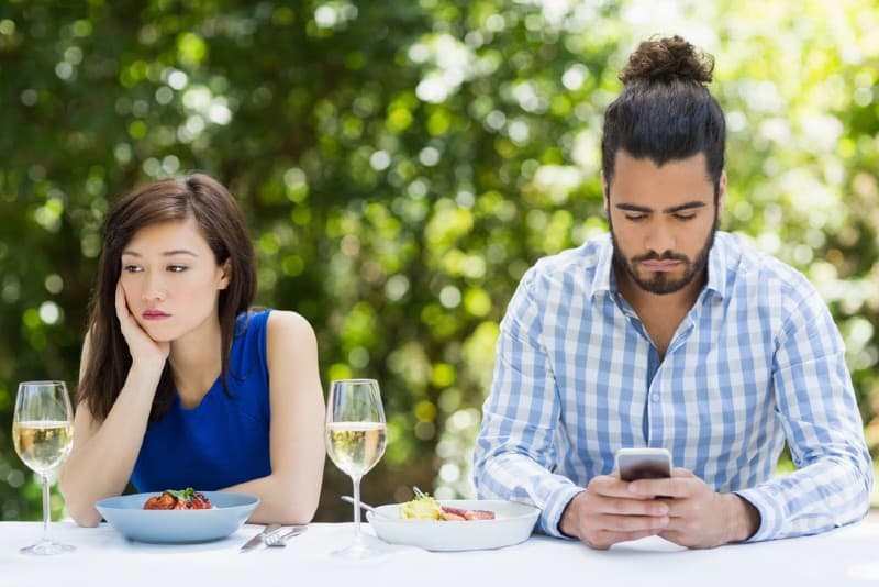 Man som ignorerar kvinnan och använder mobiltelefonen i en restaurang