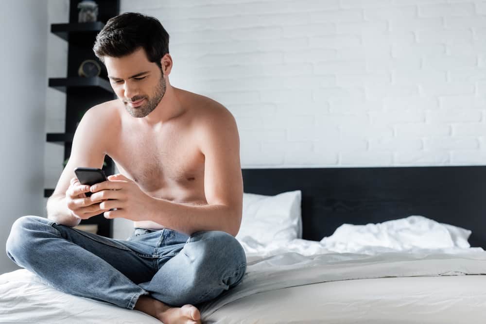 man utan skjorta med smartphone i sovrummet