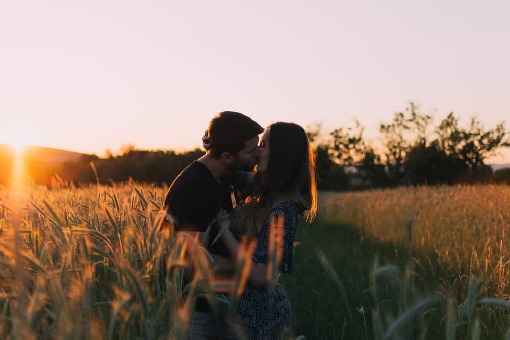 par som kysser på ängen med solnedgången i bakgrunden