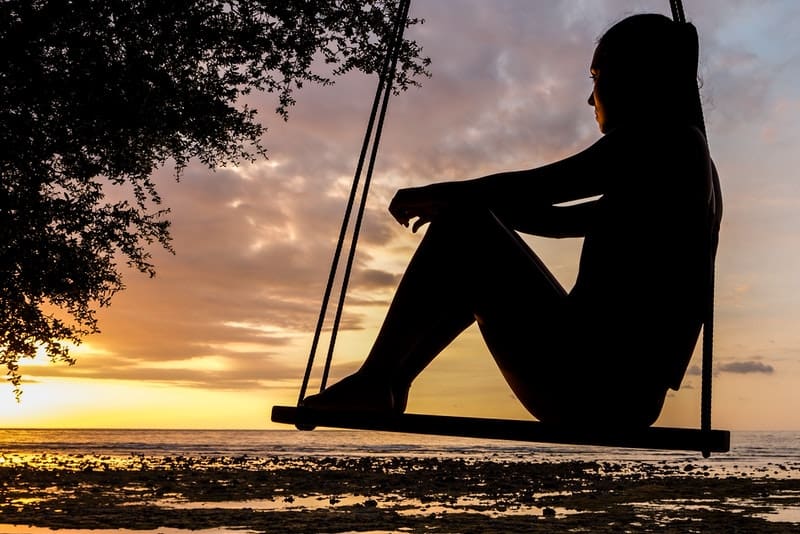 silhuett av en kvinna vid solnedgången som sitter på en gunga vid havet