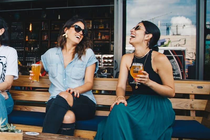 två flickor sitter och dricker öl och skrattar