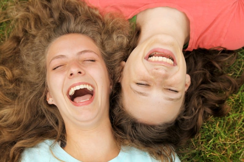 Två lyckliga tonåringvänner som ligger på ett gräs som skrattar i en park