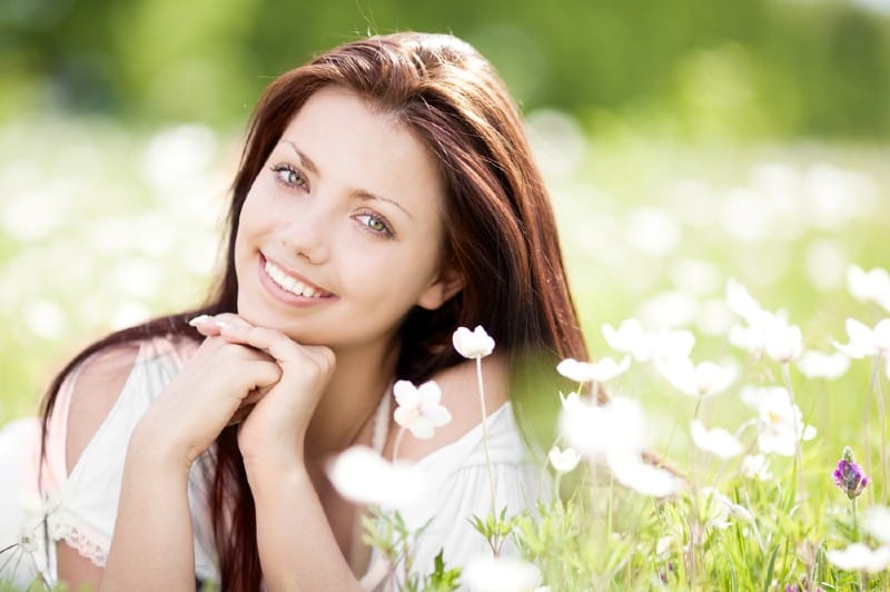 vacker ung brunettkvinna som kopplar av på ängen med vita blommor på en varm sommardag
