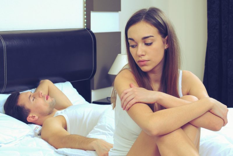 besviken kvinna som sitter på sängen medan mannen sover