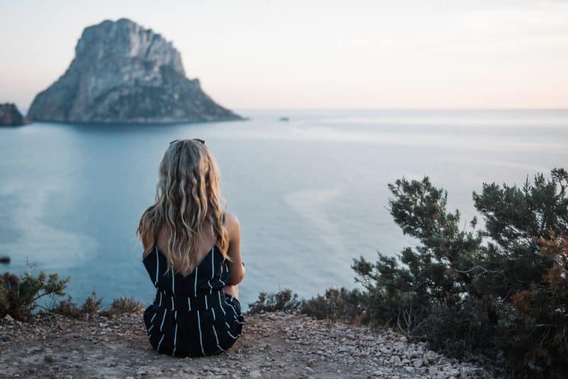 En ensam ung kvinnlig med blont hår som sitter vid havet som tycker om hennes fredliga tid