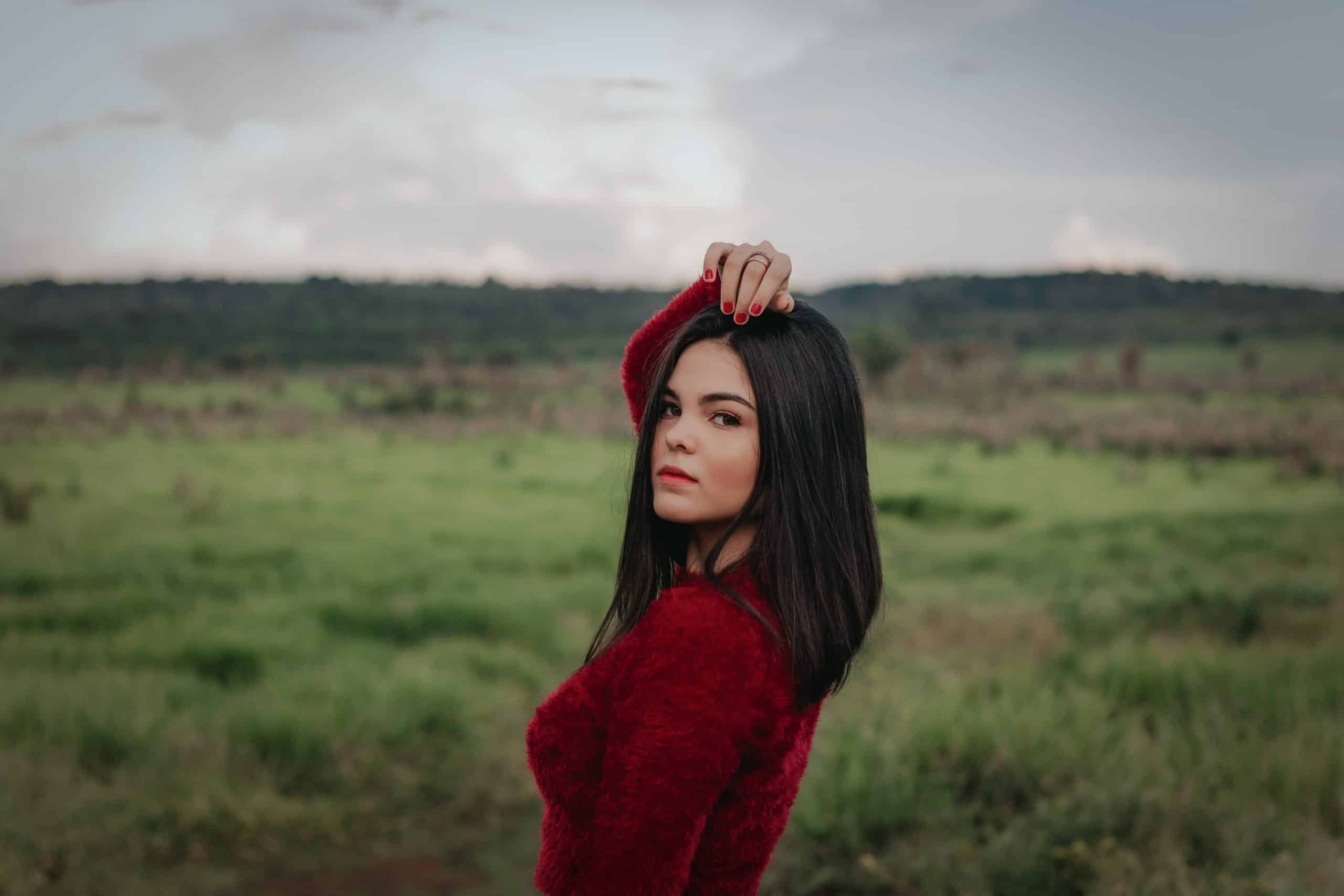 Kvinna i röd tröja som står ensam på grönt gräsfält