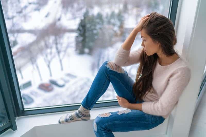 kvinna sitter ensam på fönstret och tittar på snö