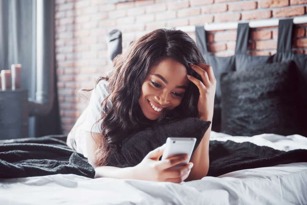 leende kvinna i sängen som håller sin telefon
