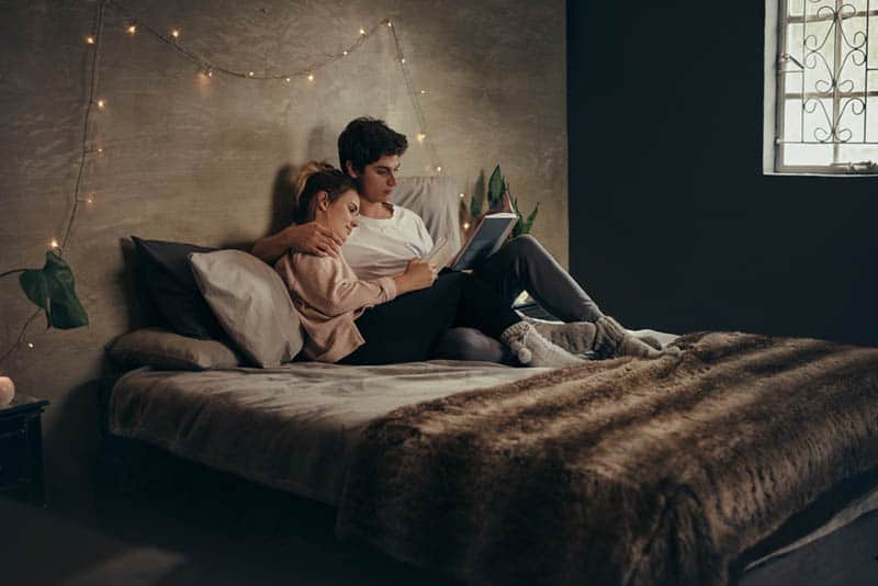 romantiska par som ligger på sängen och läser bok