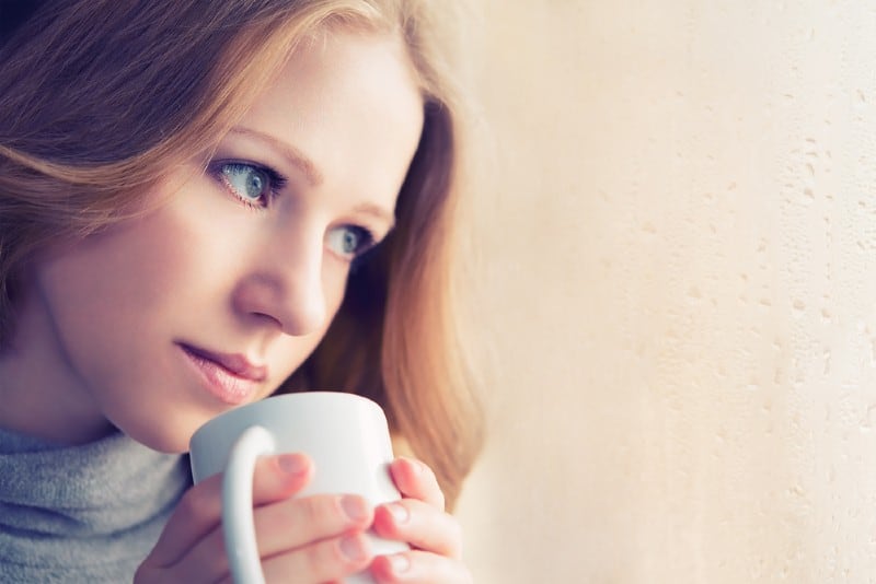 vacker drömmande tjej med en kopp varm dryck kaffe vid fönstret