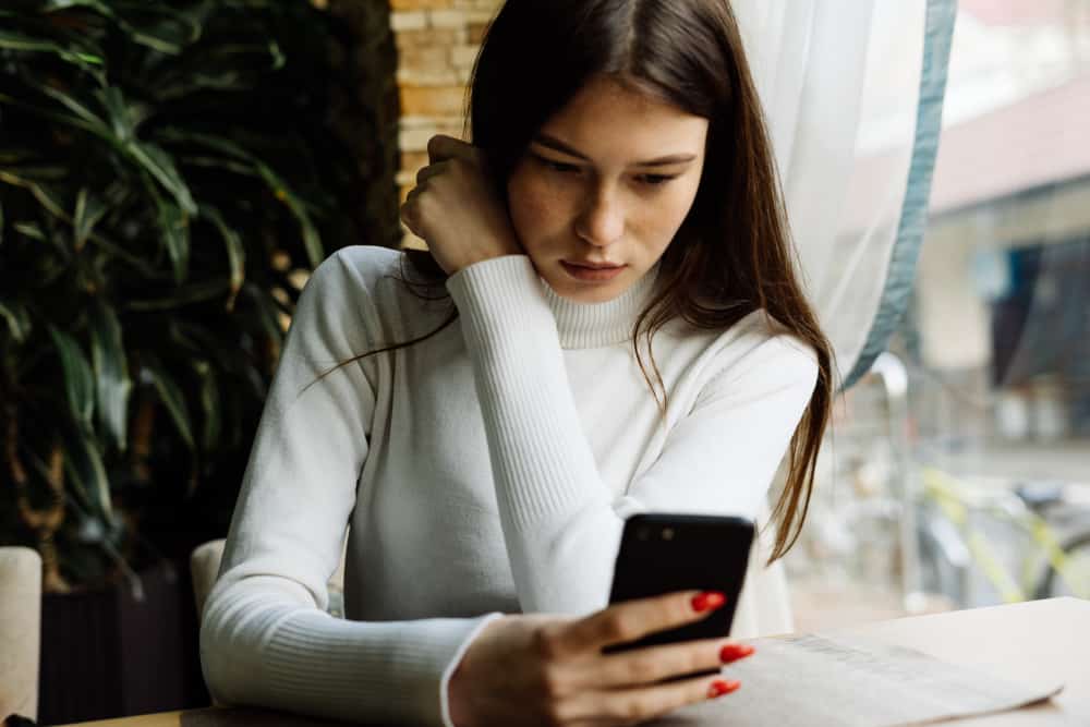 ung mörkhårig tjej i en vit tröja sitter på ett kafé och tittar i en smartphone