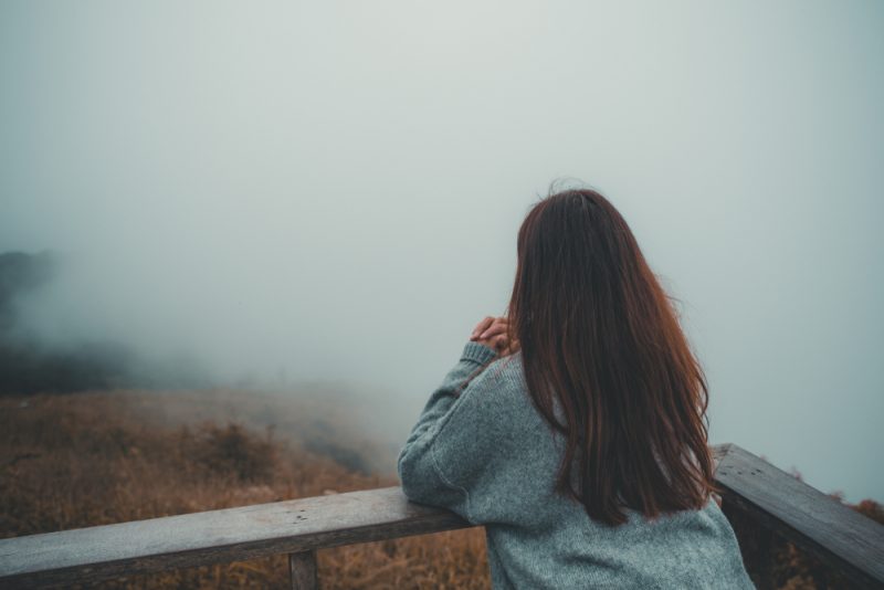 En kvinna som bara står på balkongen som ser vit dimmig och bergbakgrund