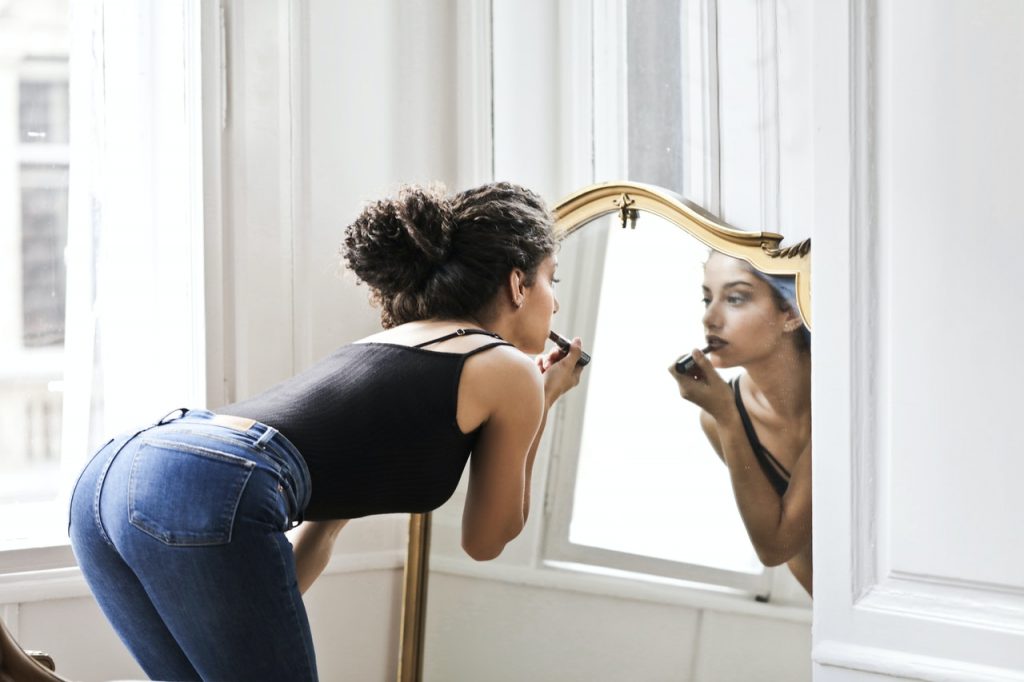 Kvinna i svart linne och blå denim som applicerar läppstift framför spegeln